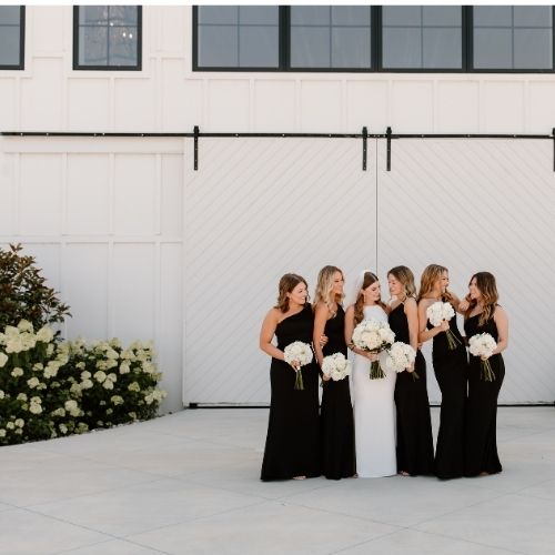 Group of bridesmaids stand with a bride while wearing one shoulder bridesmaid dresses in black satin