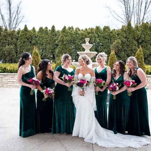 Bridal party smiles at bride while wearing emerald velvet bridesmaid dresses