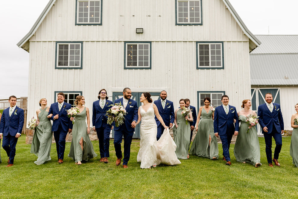 Bridal party walks away from white barn wearing Kennedy Blue bridesmaid dresses in moss green